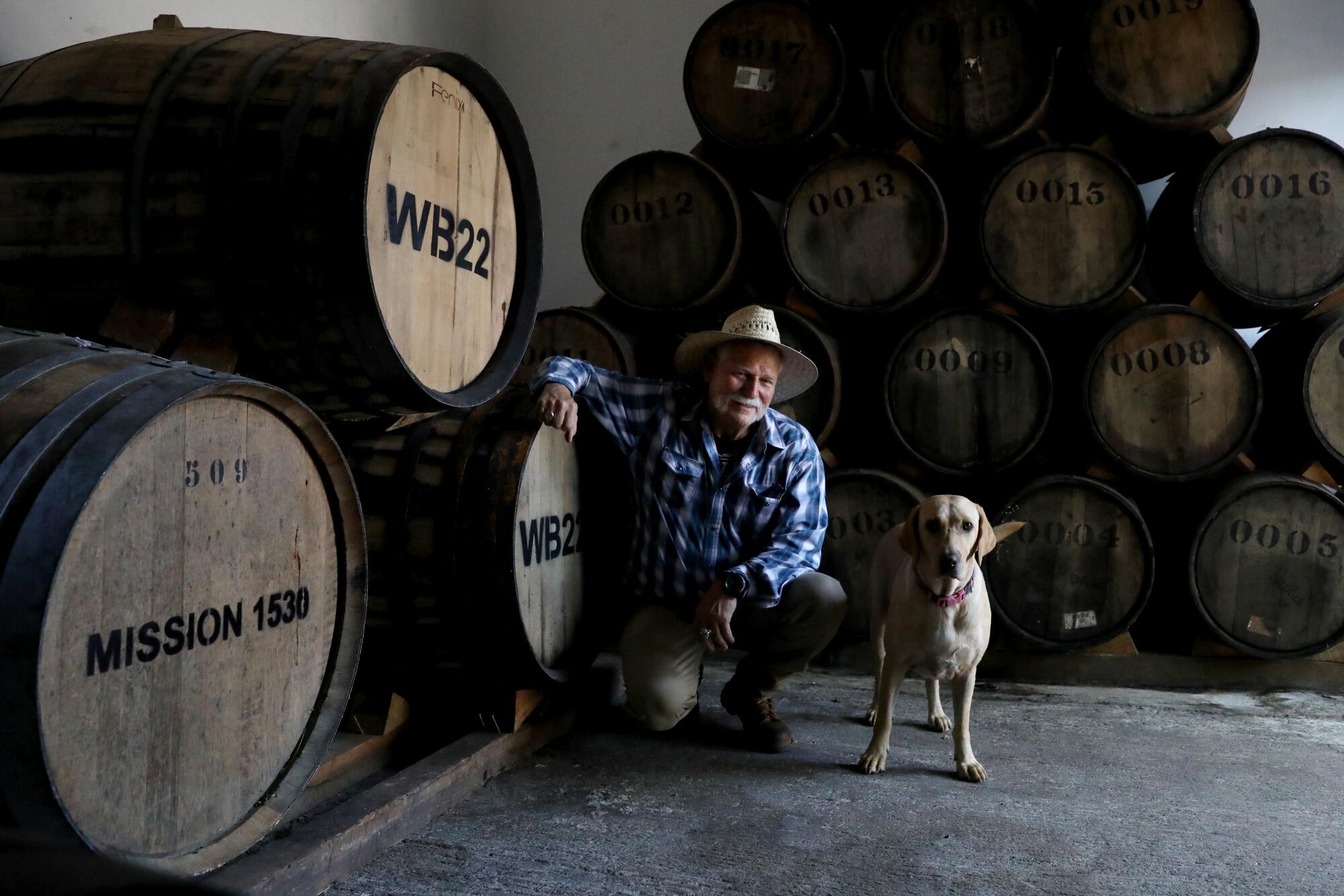 A man and his dog pose next to oak barrels