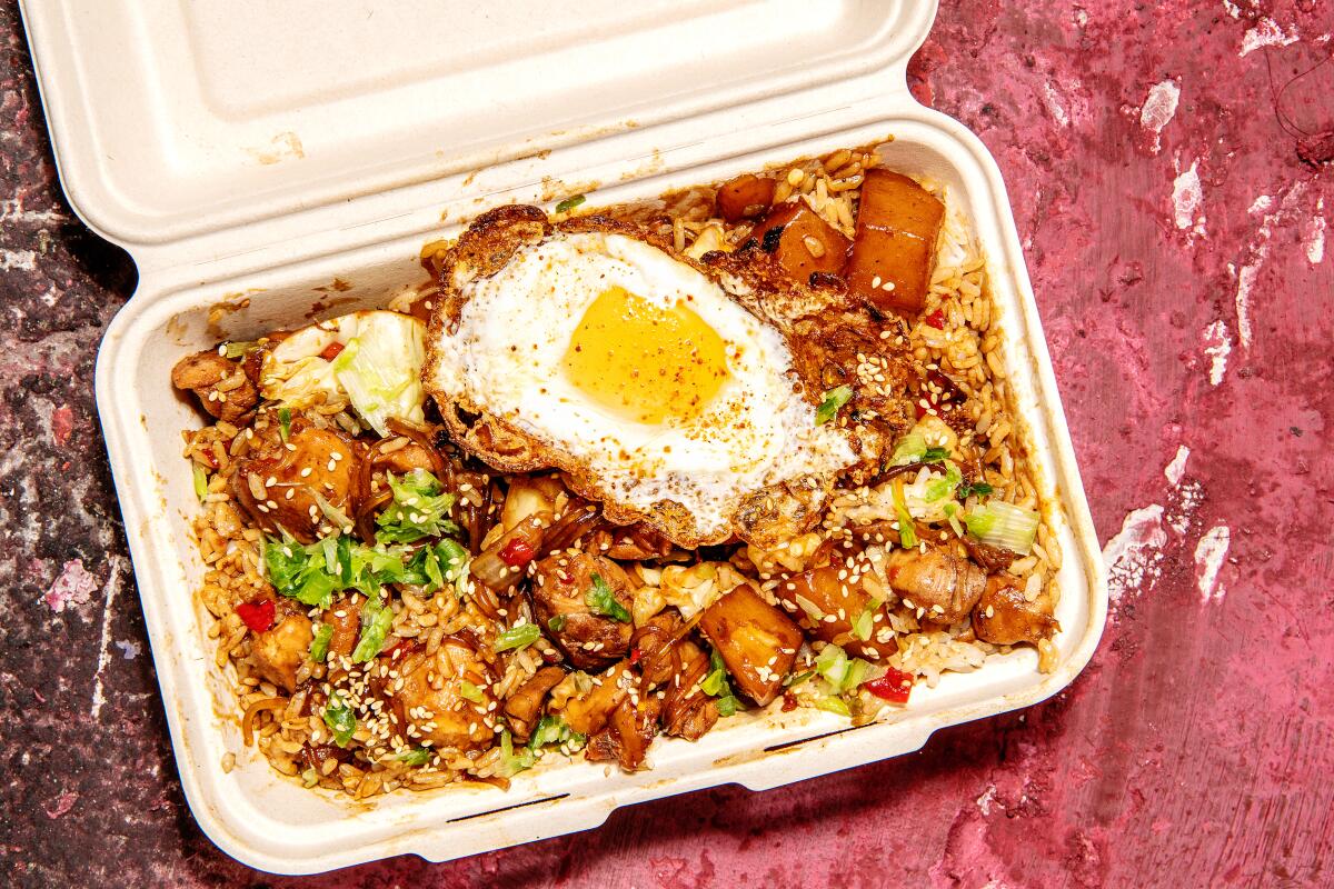 A container of meat, vegetables, rice and a fried egg. 
