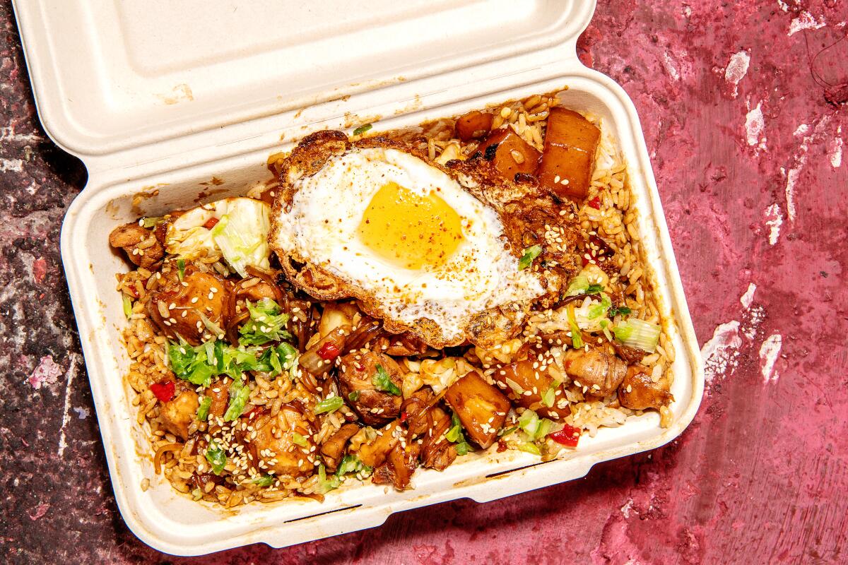 A container of meat, vegetables, rice and a fried egg.