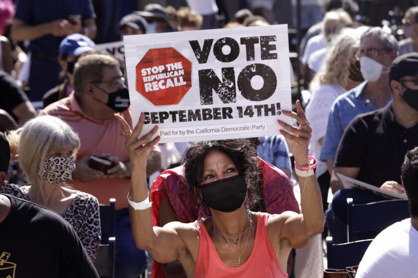 A woman holds up a sign that says Stop the Republican Recall, Vote No September 14th