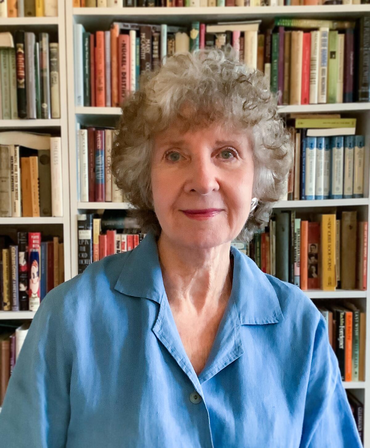 A woman in a blue blouse in front of a bookcase 