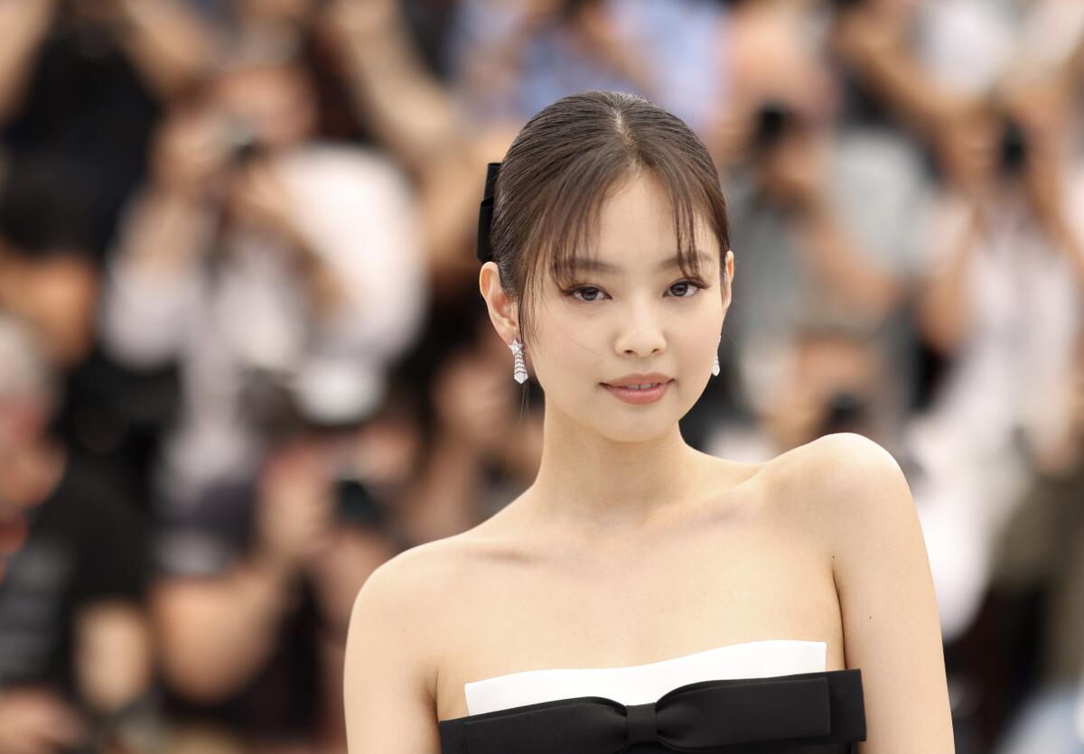 Blackpink's Jennie poses in a sleeveless black and white dress and diamond earrings with a crowd blurred out behind her.