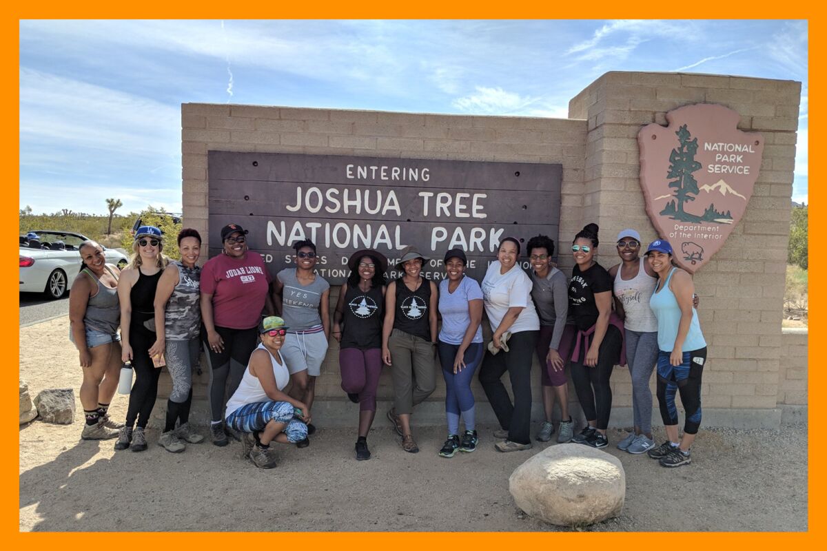 A group of hikers stands for a picture in front of the "Entering Joshua Tree National Park sign."