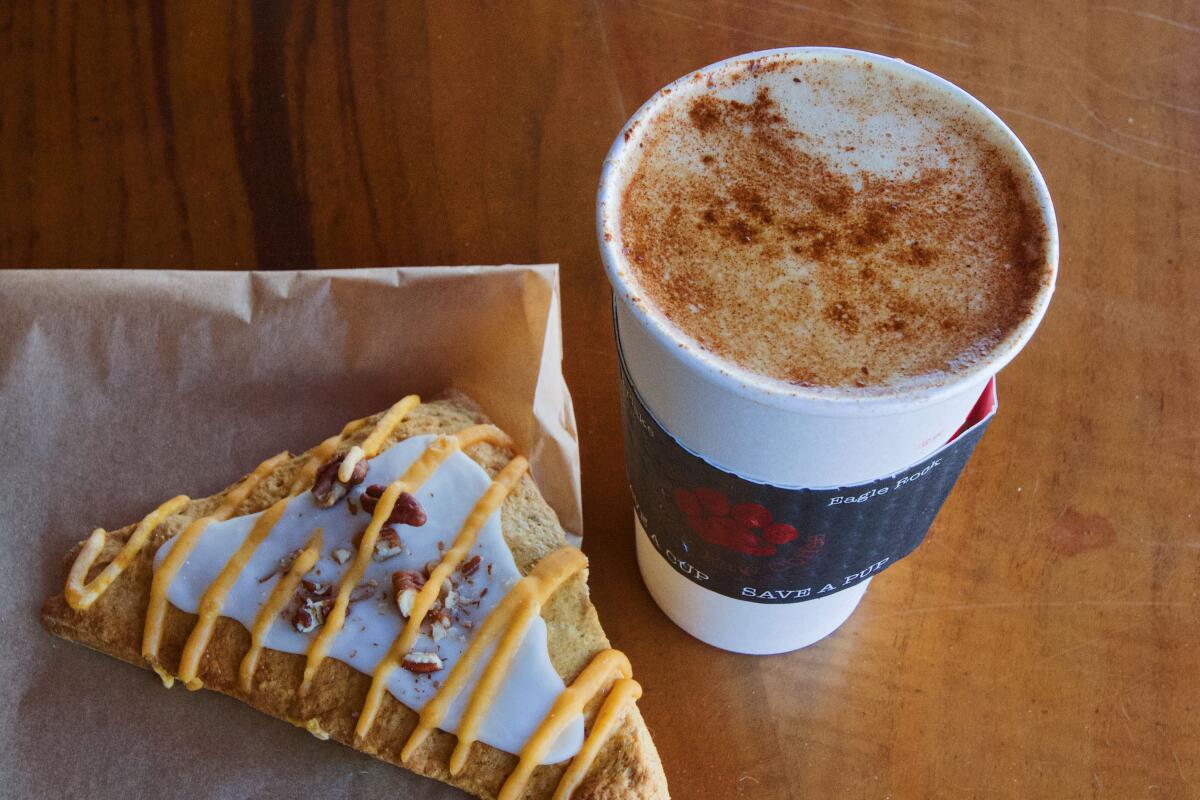 A triangular maple pumpkin scone on a wood tabletop with a large pumpkin latte in a to-go cup