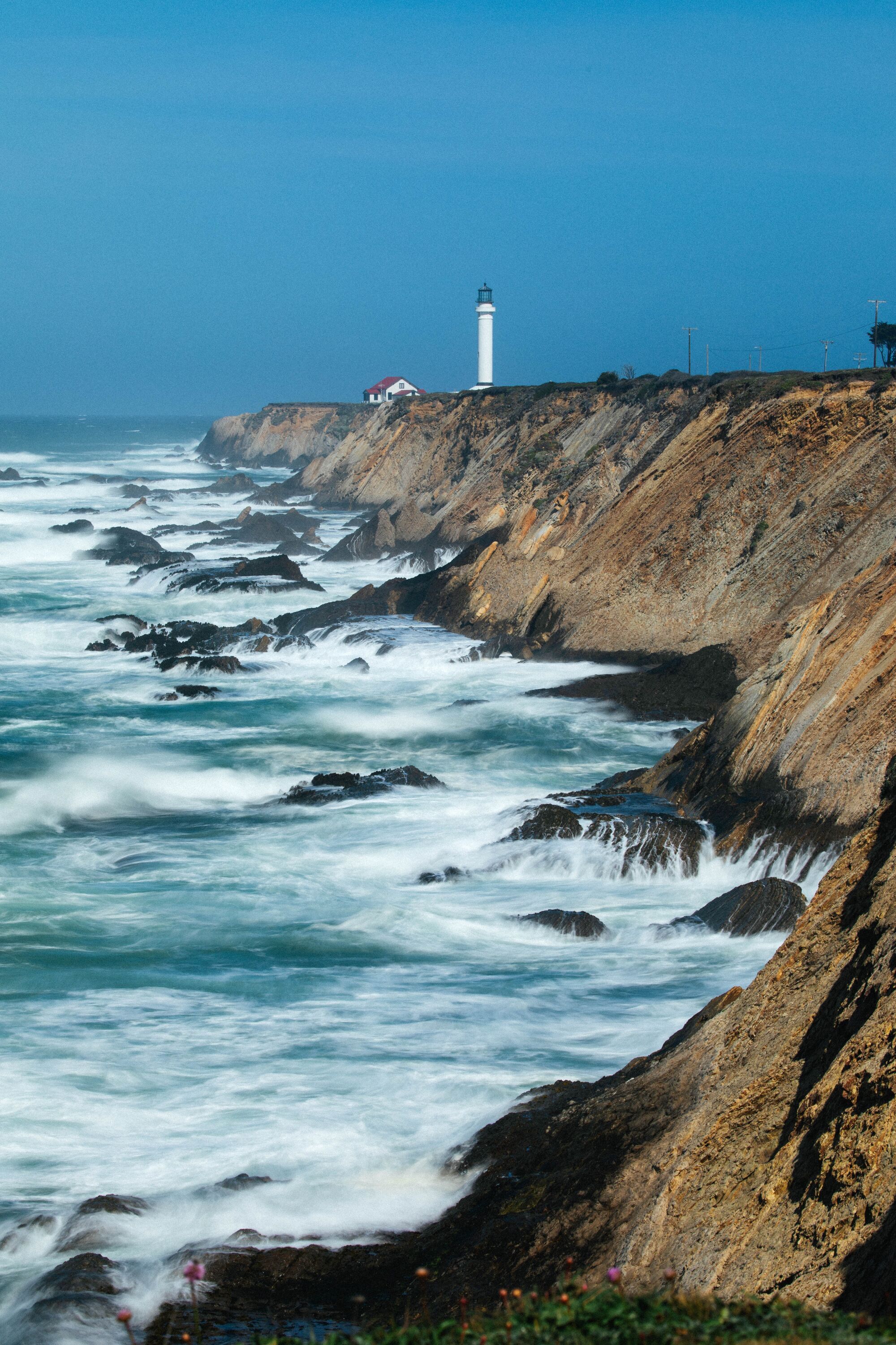 The Point Arena Lighthouse stands in the distance above a rocky seashore.