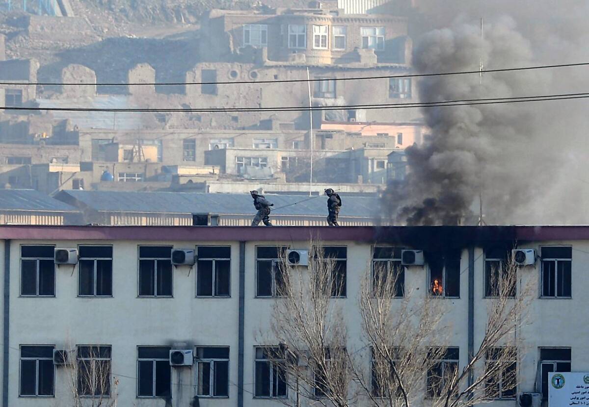 Security officers run along a rooftop at the traffic police headquarters in Kabul during a clash between Afghan forces and militants.