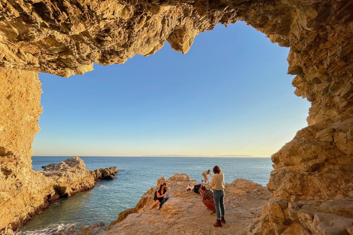 Framed by a cave entrance, people climb rocks and sit on rocks.