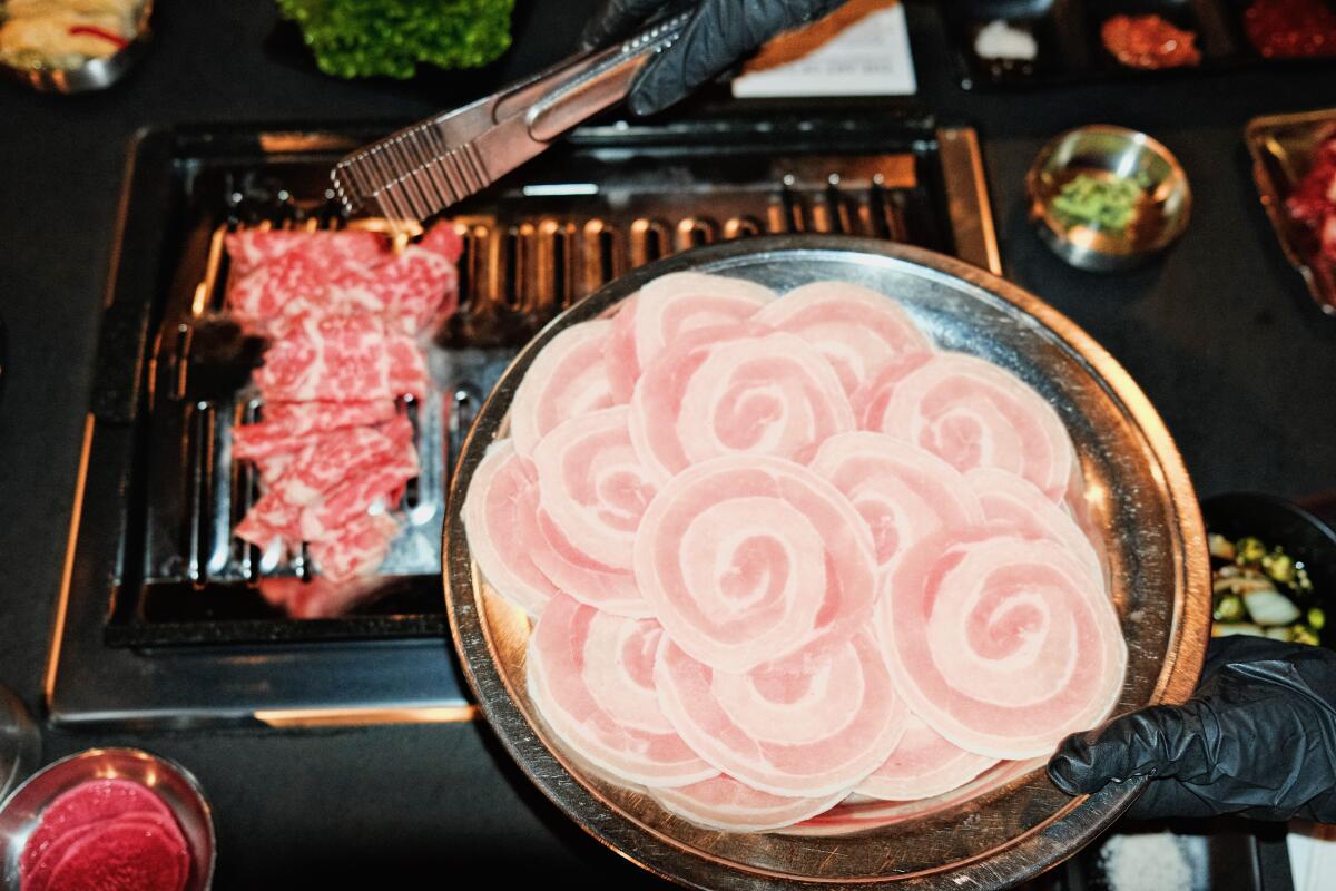 A platter of raw disks of pork belly next to a grill with meat.