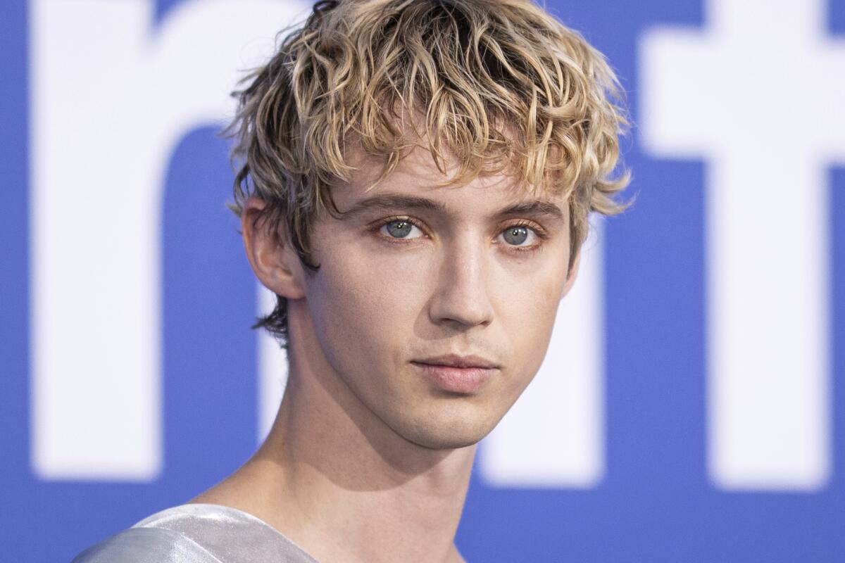 Troye Sivan posing against a blue background.