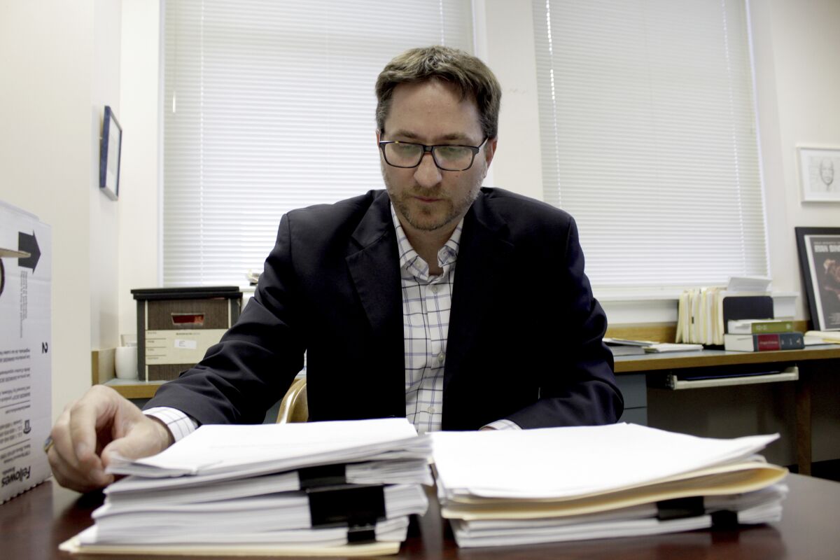 Carl Macpherson, executive director at Metropolitan Public Defender, examines the file in a double murder case that was recently pushed back for trial in his office in Portland, Ore., on May 5, 2022. Macpherson says his firm of 90 public defenders recently stopped taking certain types of new criminal cases for a month in two local courts because they had so many cases that the attorneys were violating their ethical obligations to clients. A post-pandemic glut of delayed cases has exposed shocking constitutional landmines impacting defendants and crime victims alike in Oregon, where an acute shortage of public defenders has even led judges to dismiss serious cases. (AP Photo/Gillian Flaccus)