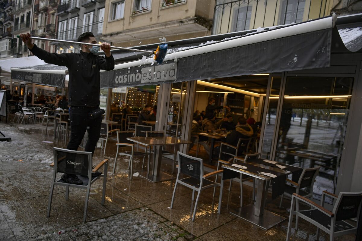 A worker wearing a face mask clears snow from the roof of a bar, in Pamplona, northern Spain, Saturday, Dec. 5, 2020. (AP Photo/Alvaro Barrientos)
