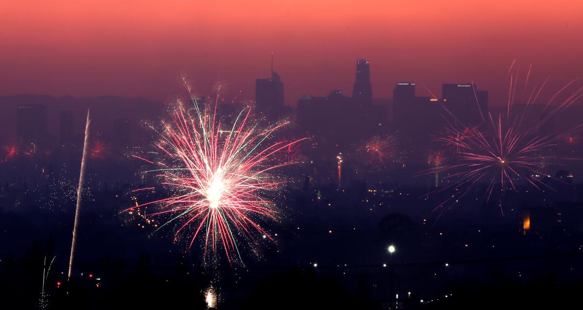 Downtown Los Angeles can be seen in the background through haze and smoke with Fourth of July fireworks going off 