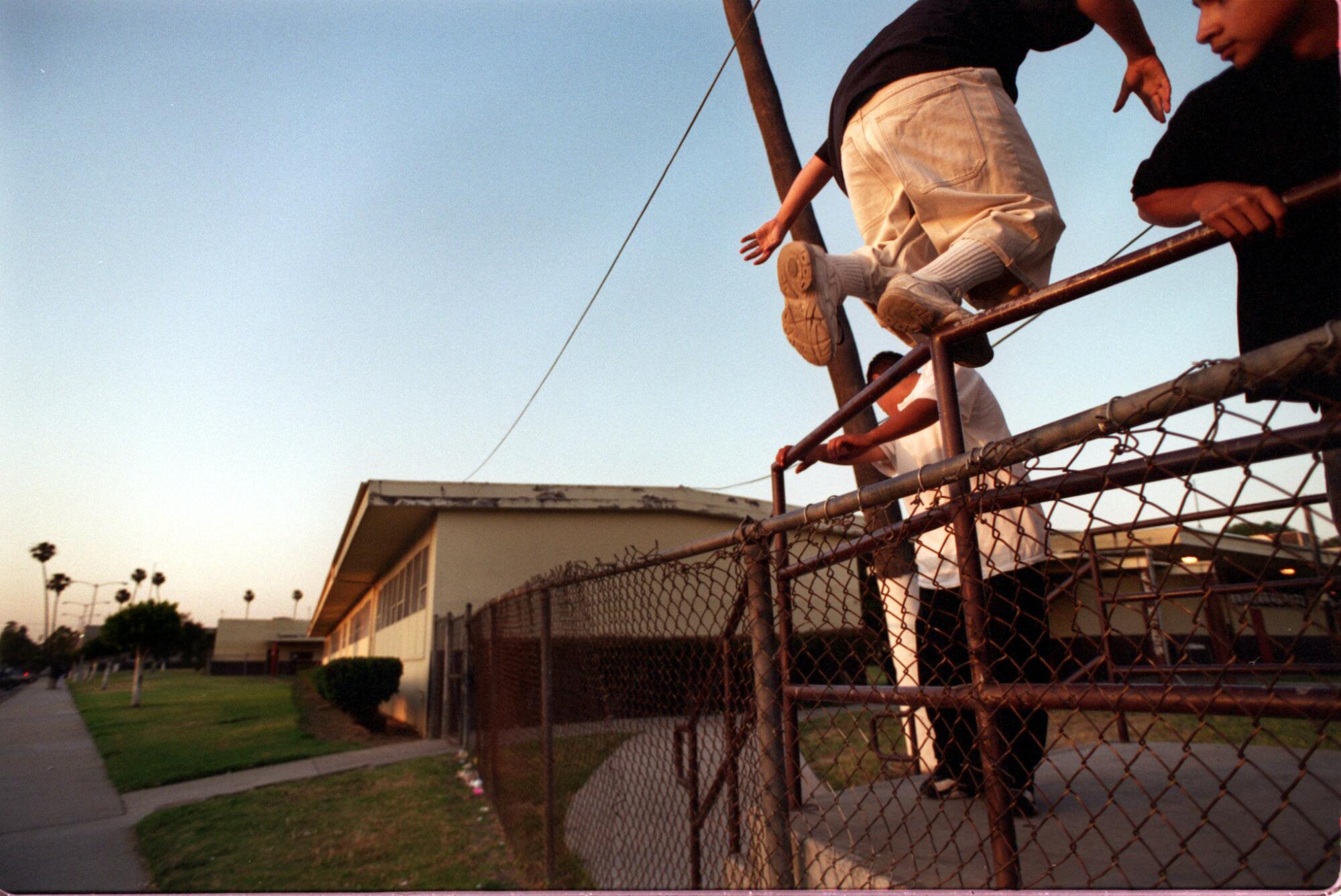 Three young men, wearing black and white, hop a fence.