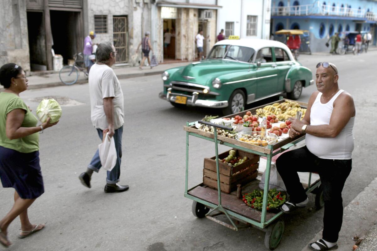 Un vendedor callejero de frutas ofrece sus productos en una calle de La Habana, con un auto de los años 50 de fondo, en foto del 3 de diciembre del 2013. Si viaja a Cuba lleve dinero en efectivo y tenga en cuenta que hay pocos sitios donde cambiarlo por pesos cubanos y que casi no se aceptan tarjetas de crédito de Estados Unidos.