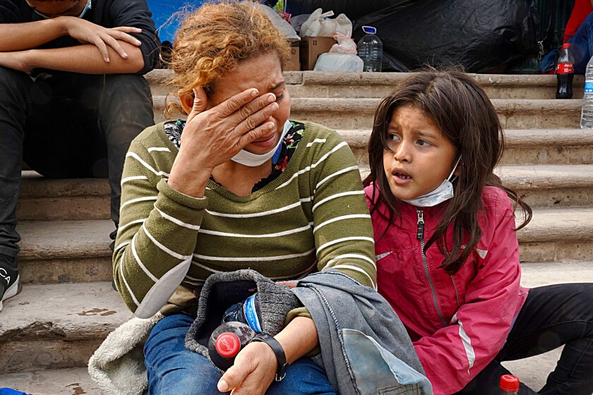 A woman with her hand over her face and a child sit on steps