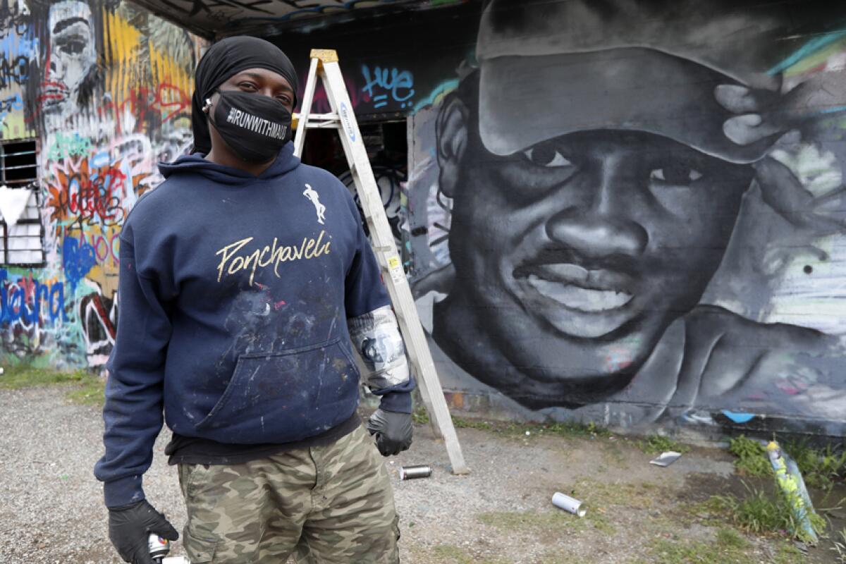 Artist Theo Ponchaveli stands next to a mural of Ahmaud Arbery in Dallas.