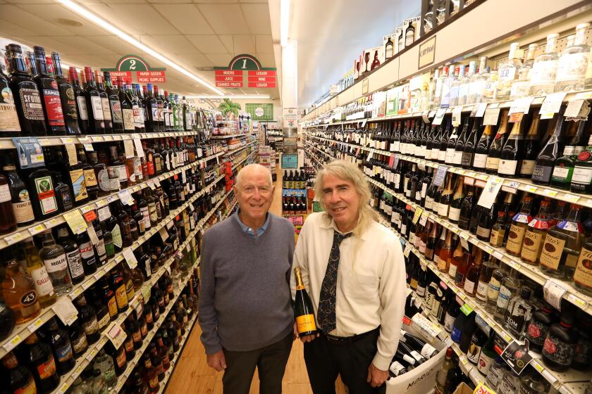 SANTA MONICA, CA - DECEMBER 8, 2021 - Bob Rosenbloom, 89, left, owner of Bob's Market, and his son Rick, 66, holding a $69.99 bottle of Cliquot champagne, stand in the wine and alcohol section of Bob's Market in Santa Monica on December 8, 2021. Rick Rosenbloom purchases the wine for the market. With the availability of alcoholic beverages being reduced due to the situation at the port, some prices are going up. The Rosenbloom's have been fighting a sometimes losing battle to keep price hikes at bay. They have a substantial selection of wines, champagne and hard liquor available at the store. The Cliquot champagne prices have risen from $55 recently to $69.99 a bottle. (Genaro Molina / Los Angeles Times)