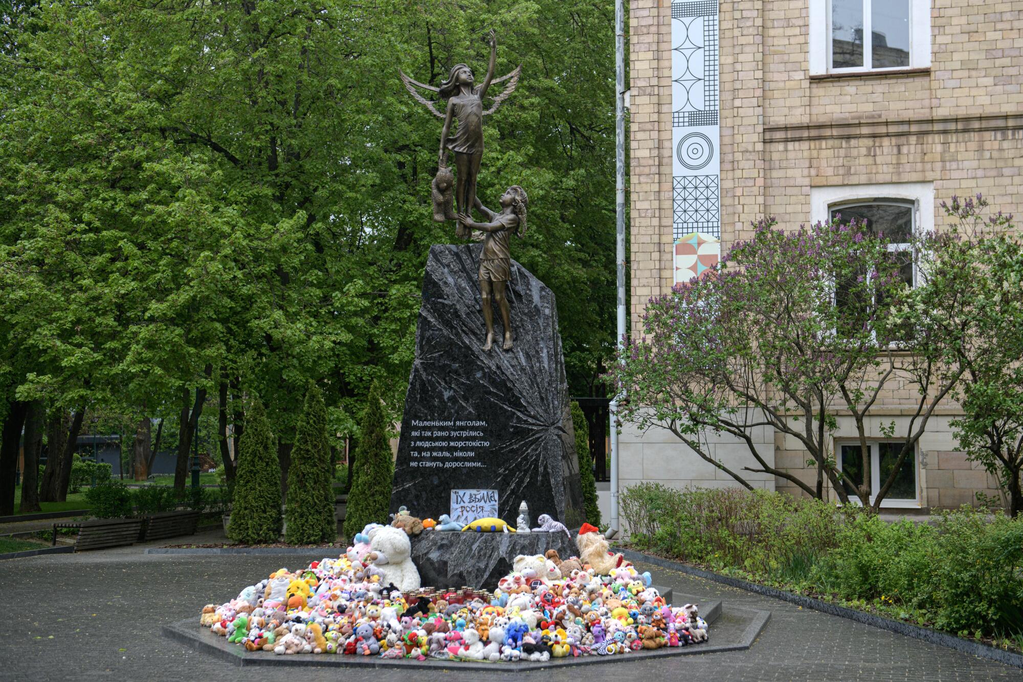 Teddy bears surround a monument in front of a building, near leafy trees