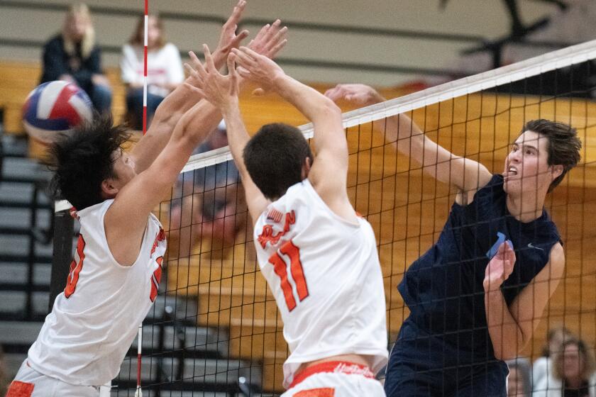 Corona del Mar's Sterling Foley hits off the block of Huntington Beach's Colin Choi, left, and Logan Hutnick (11) during the CIF State Southern California Regional Division I playoffs at Huntington Beach High on Tuesday.