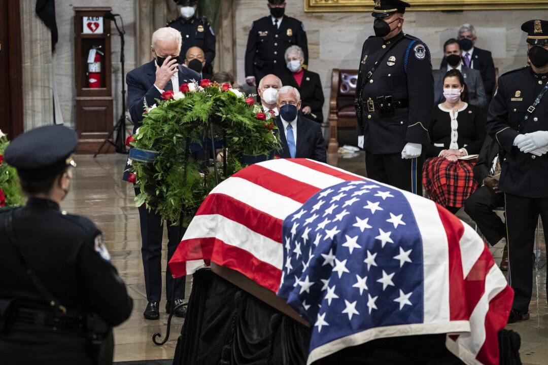 پرزیدنت جو بایدن روی تریبون در کنار تاج گل و تابوت سناتور باب دول (کانزاس) که با پرچم ایالات متحده پوشیده شده است، ایستاده است. 