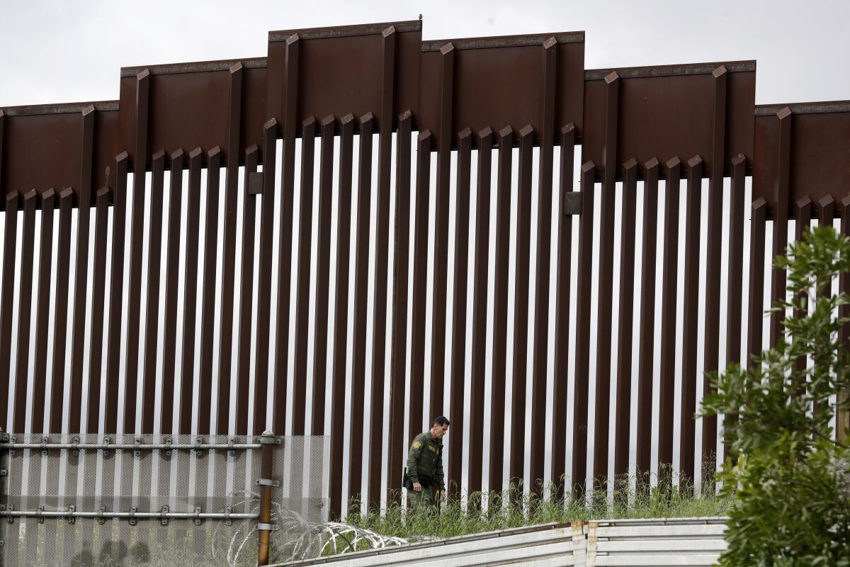 FILE - In this March 18, 2020, file photo, a Border Patrol agent walks along a border wall separating Tijuana, Mexico, from San Diego, in San Diego. U.S. authorities wield extraordinary power available in public health emergencies, like the coronavirus pandemic, to expel Mexicans and many Central Americans immediately to Mexico and waive immigration laws that include rights to seek asylum. (AP Photo/Gregory Bull, File)