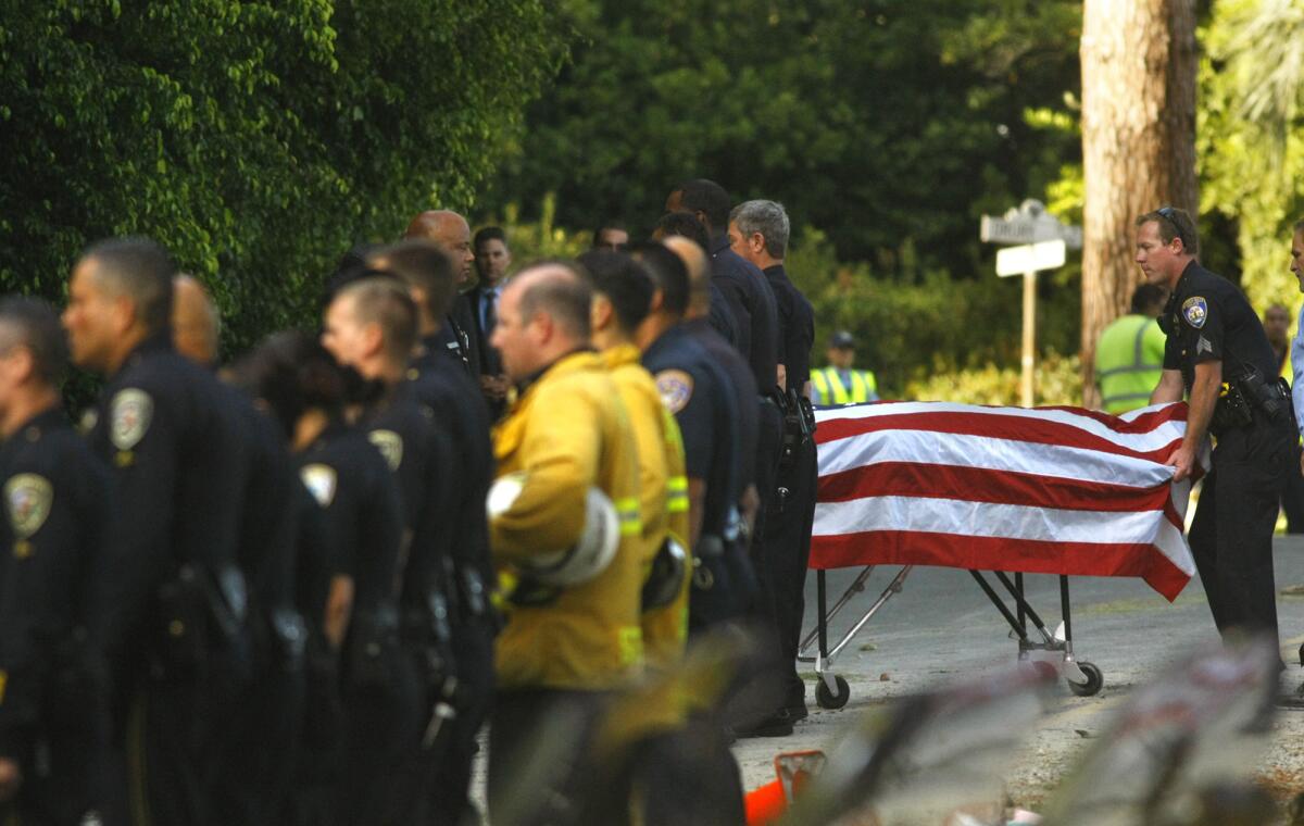 A police officer pulls the gurney carrying the body of an off-duty police officer killed in an accident with a cement truck on Loma Vista Drive in Beverly Hills.