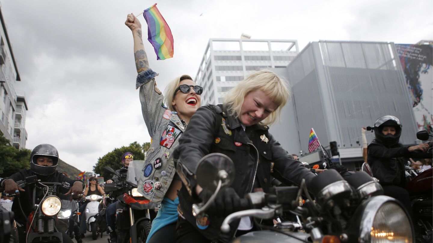 Kristen Wright, 36, thrusts a gay pride flag into the sky as Ashley Boyd, 30, rides a motorcycle