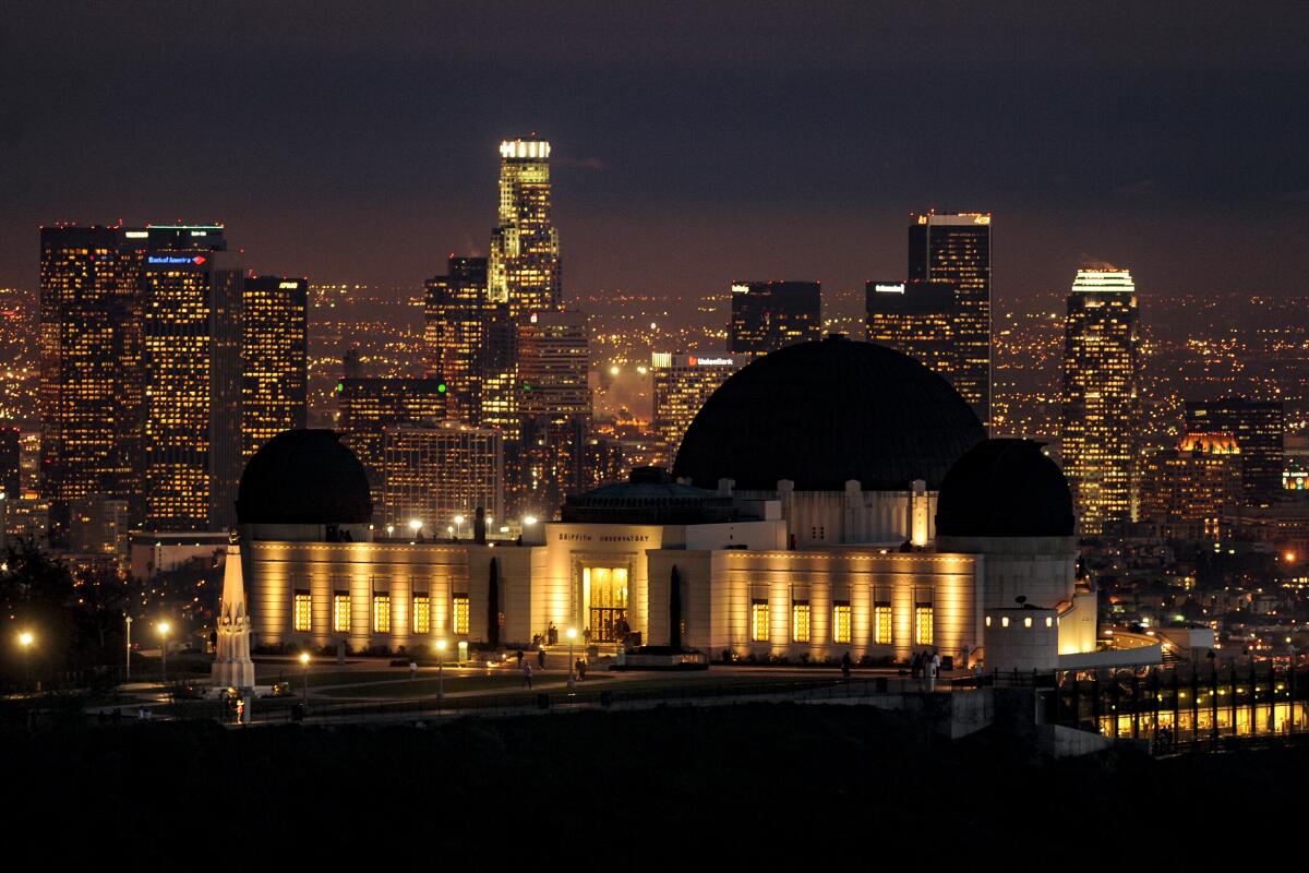 Griffith Observatory is lit up at night, with the Los Angeles skyline behind it.