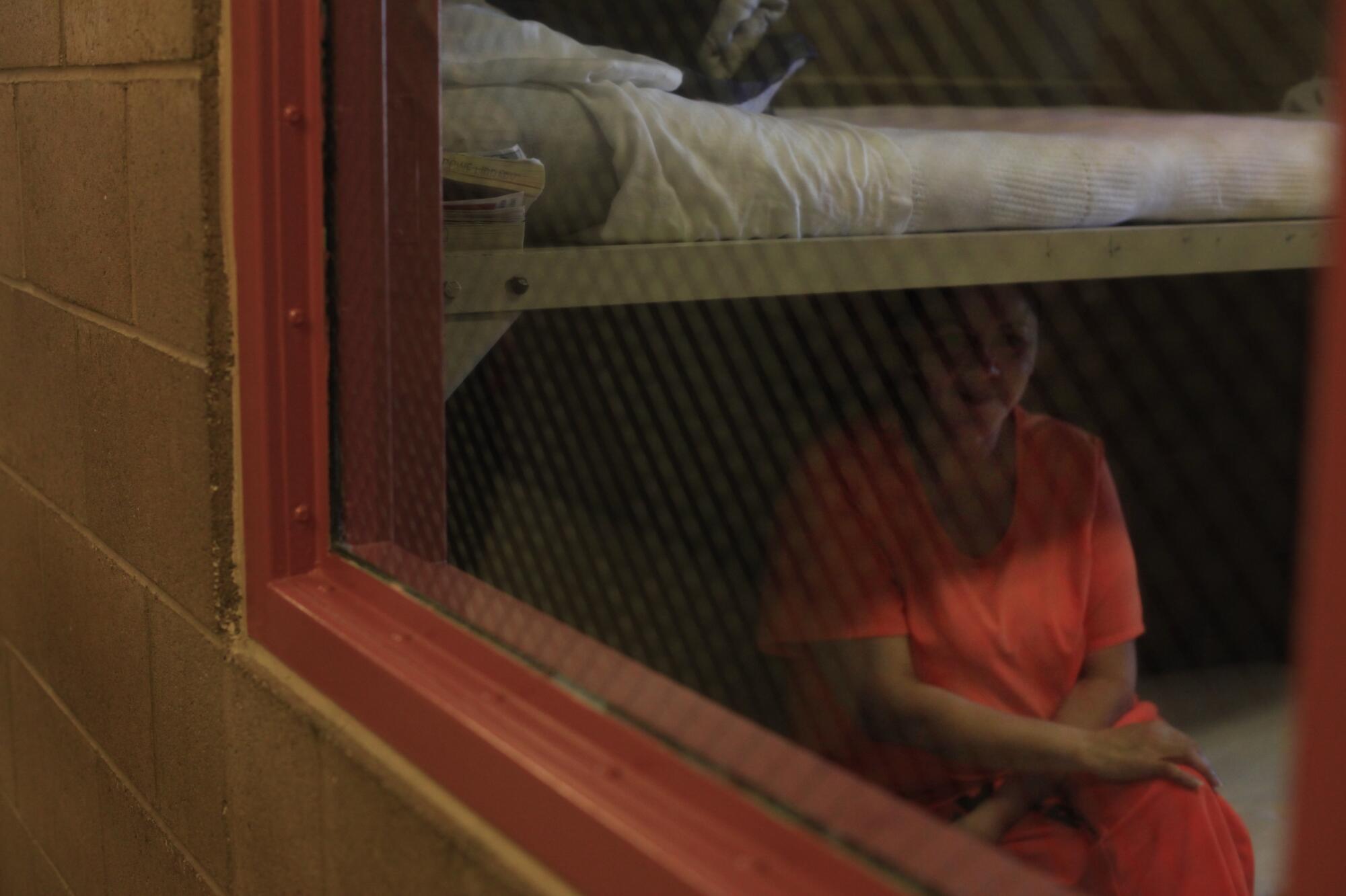 A prison inmate sits on a bunk.