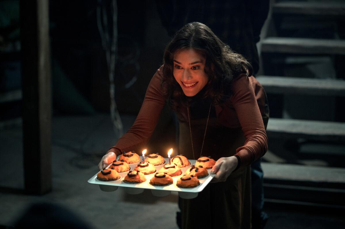 A mother smiles, holding a tray of candlelit cupcakes.