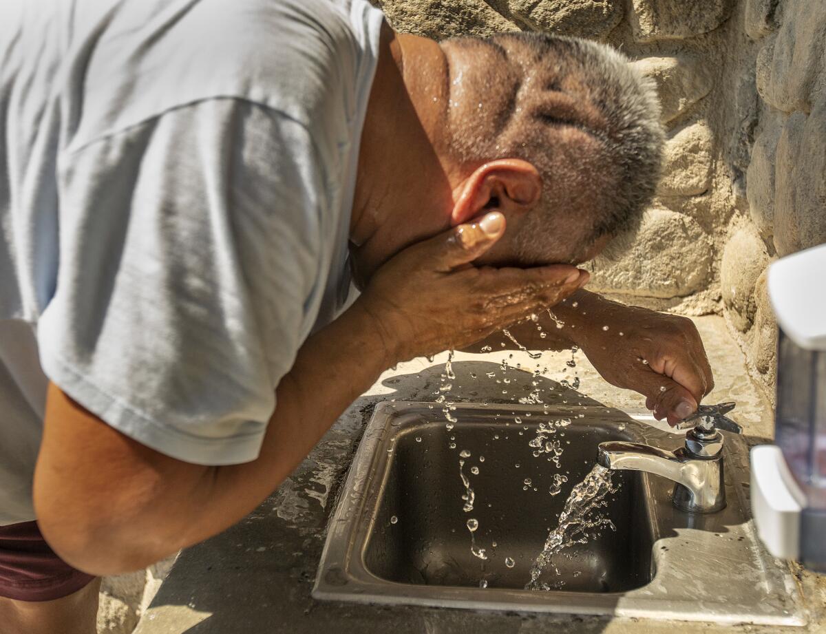 A man washes his face at an outdoor sink.