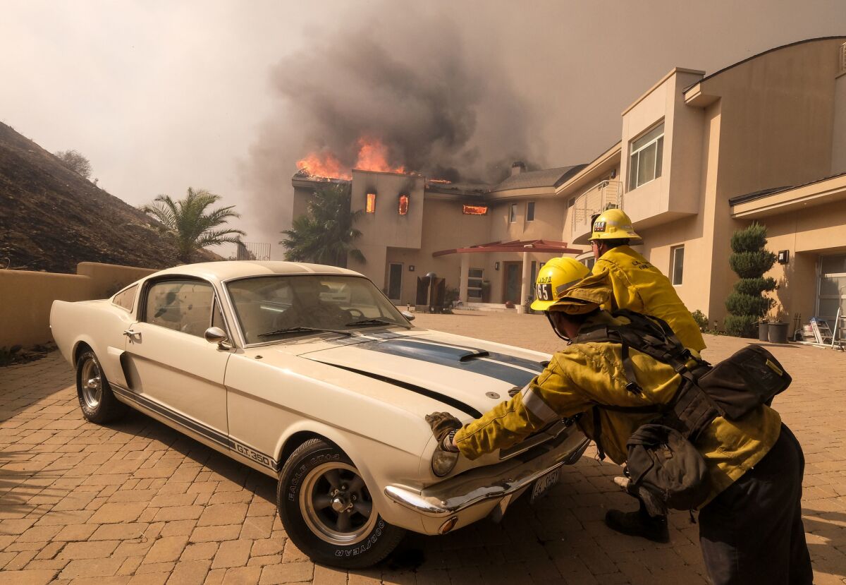 Firefighters push a vehicle from a garage as the Woolsey fire burns a home near Malibu Lake on Nov. 9.