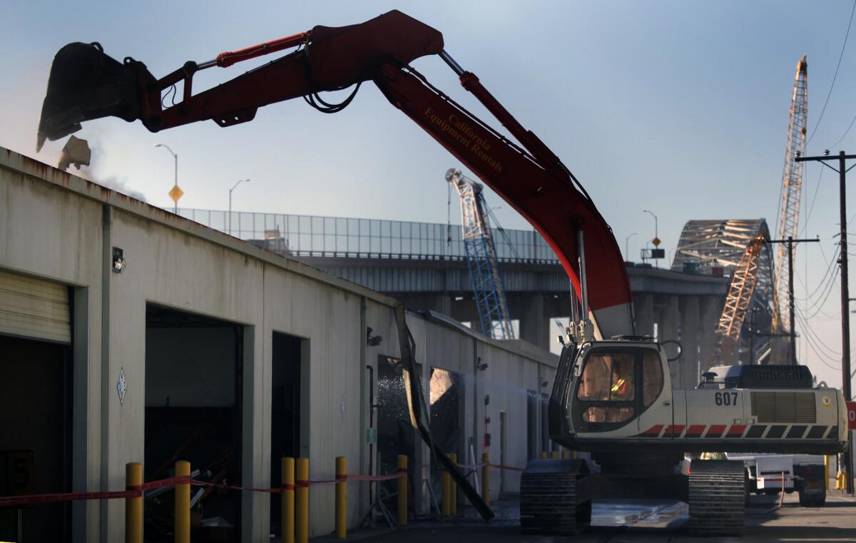A building in an old port maintenance yard is demolished Thursday to make way for a new six-lane bridge at the Port of Long Beach as part of the Gerald Desmond Bridge Replacement Project.
