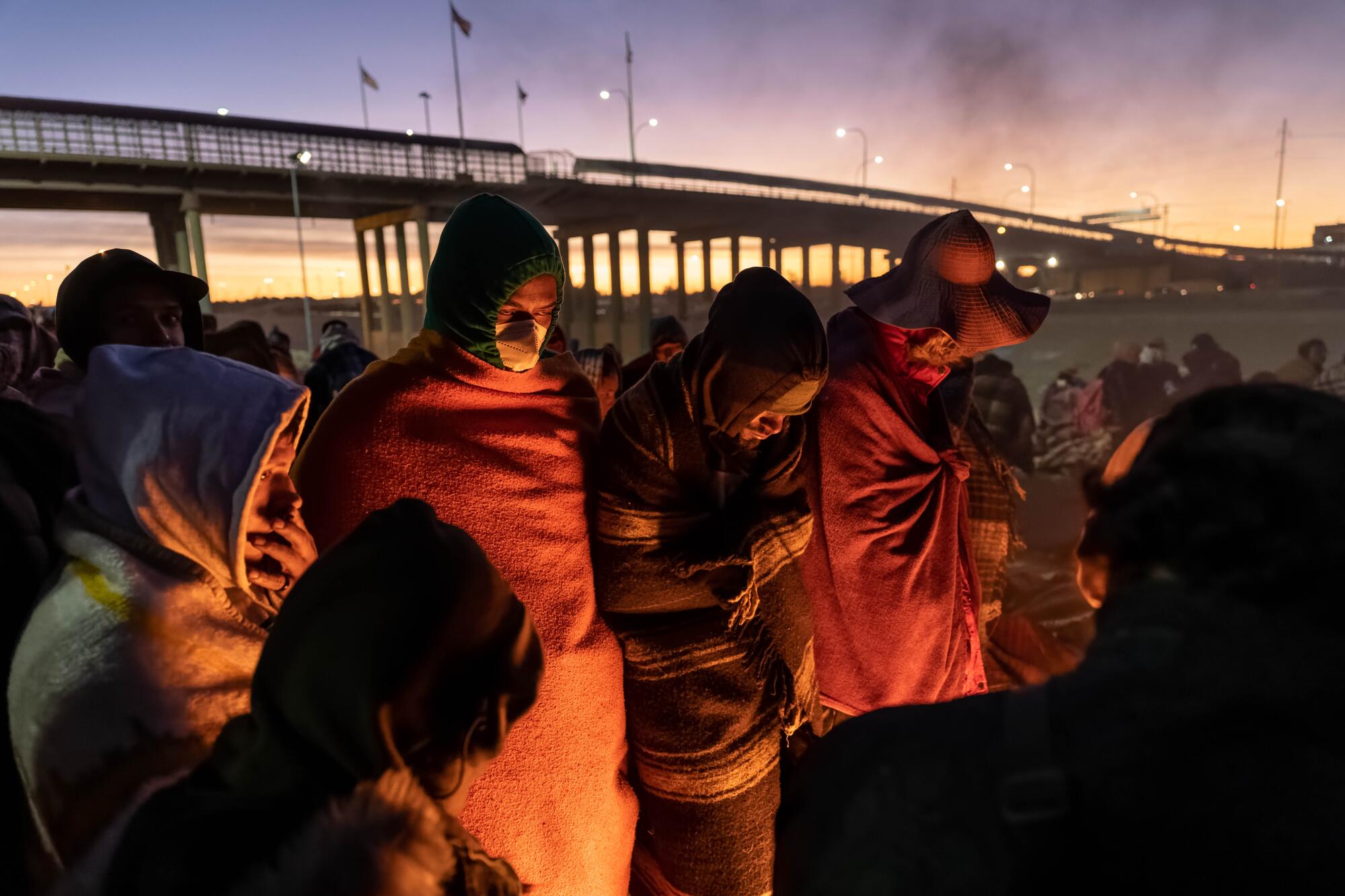 Migrants this week in El Paso wrap themselves in blankets and warm themselves by a fire at dawn.
