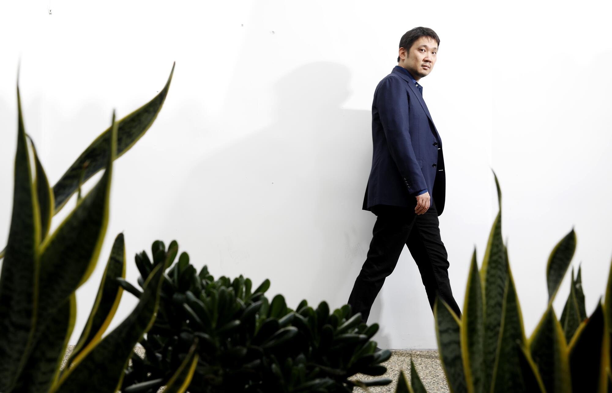 Ryûsuke Hamaguchi walks next to some outdoor plants.