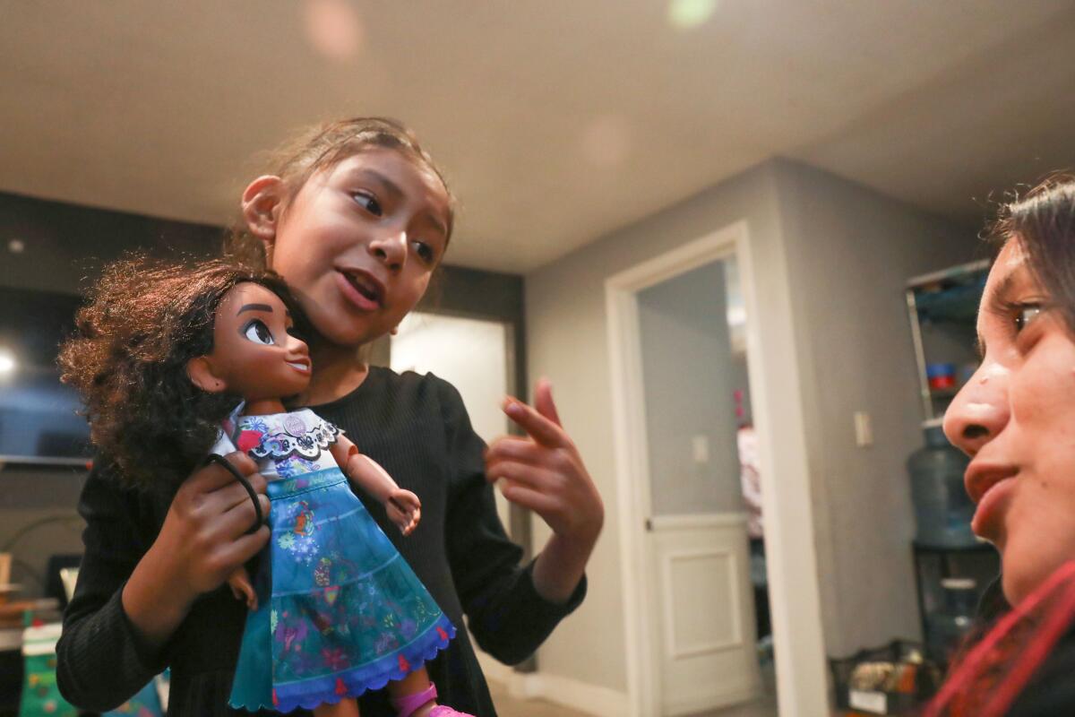 A girl holds a doll while talking to her mother. 