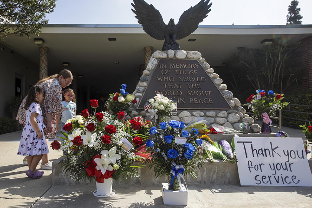 A woman and two girls next to flowers around an eagle statue with the words "In memory of those who served"