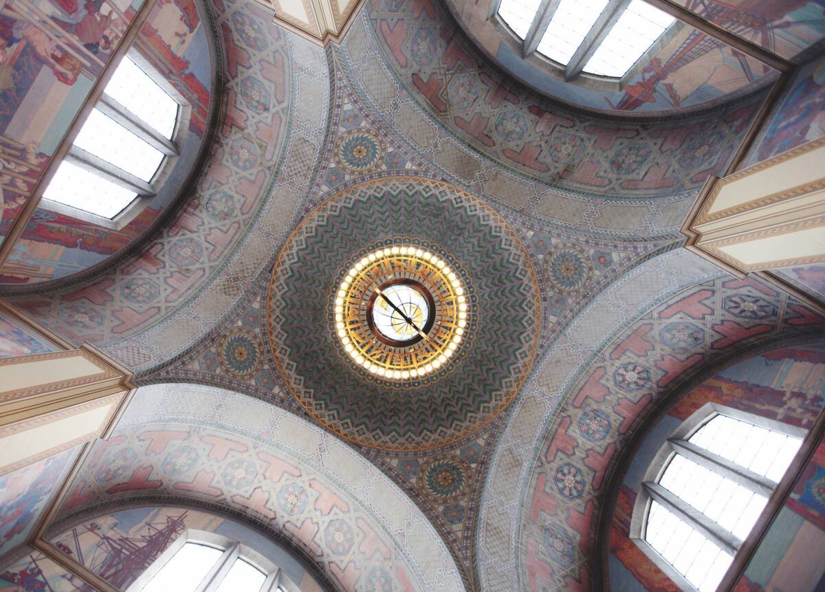 The rotunda ceiling of the L.A. Central Library, with its bronze Zodiac Chandelier, stenciling painted directly on the concrete and murals of California history. (Angel City Press)