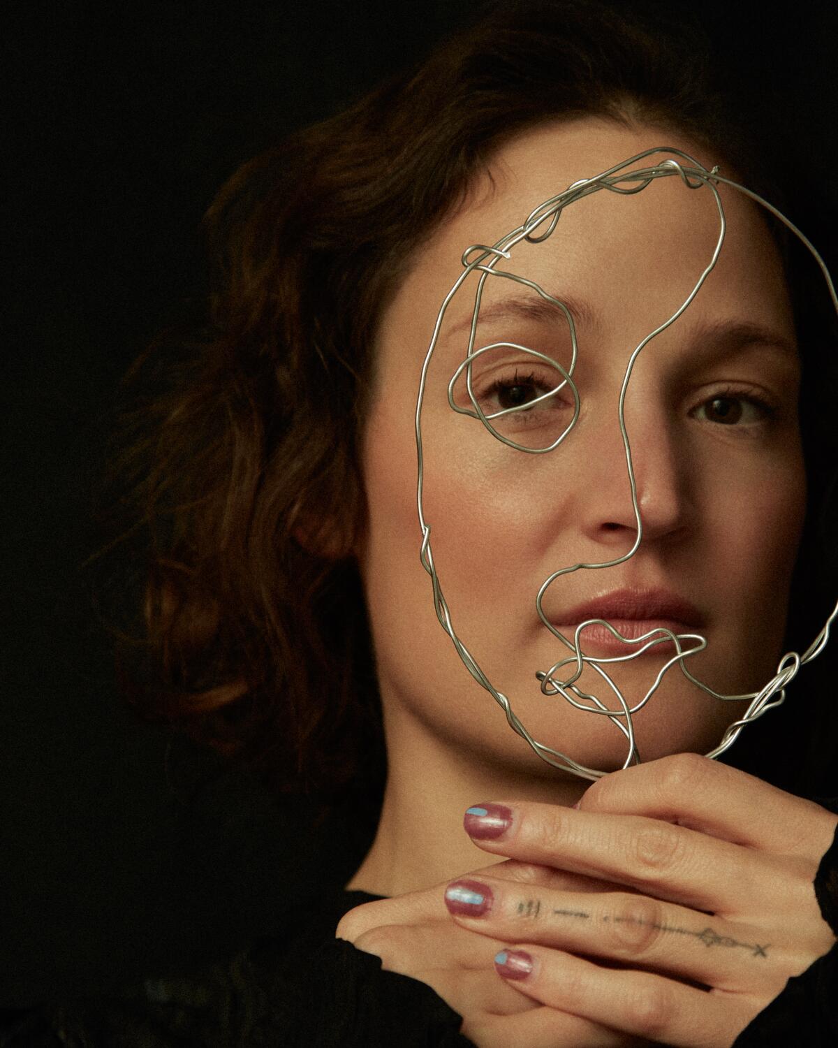 A woman holds a wire sculpture up to her face and looks through it. 