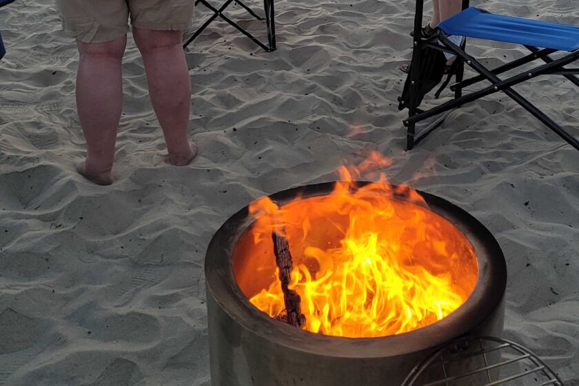 Beachgoers on Mission Beach gather around a portable fire pit to watch an early summer sunset last week. 