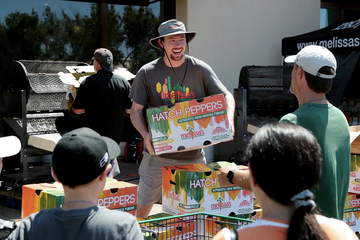 Travis Peugh, center, hands a customer a box of Melissa's roasted Hatch chiles.
