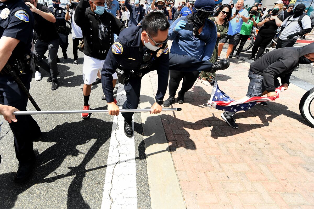 A police officer tries to intervene as a young man takes an American flag from a demonstrator