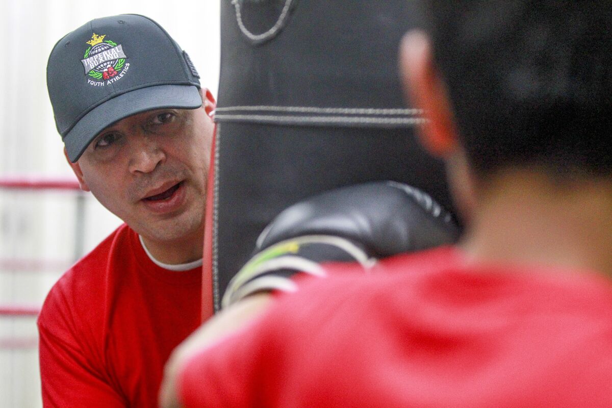 Imperial Boxing Youth Athletics Club's founder Ruben Gutierrez, a San Diego Police lieutenant, holds a punching bag for one of the boys in his boxing club at the Dolores Magdaleno Recreation Center in Logan Heights on Thursday, December 19, 2019.