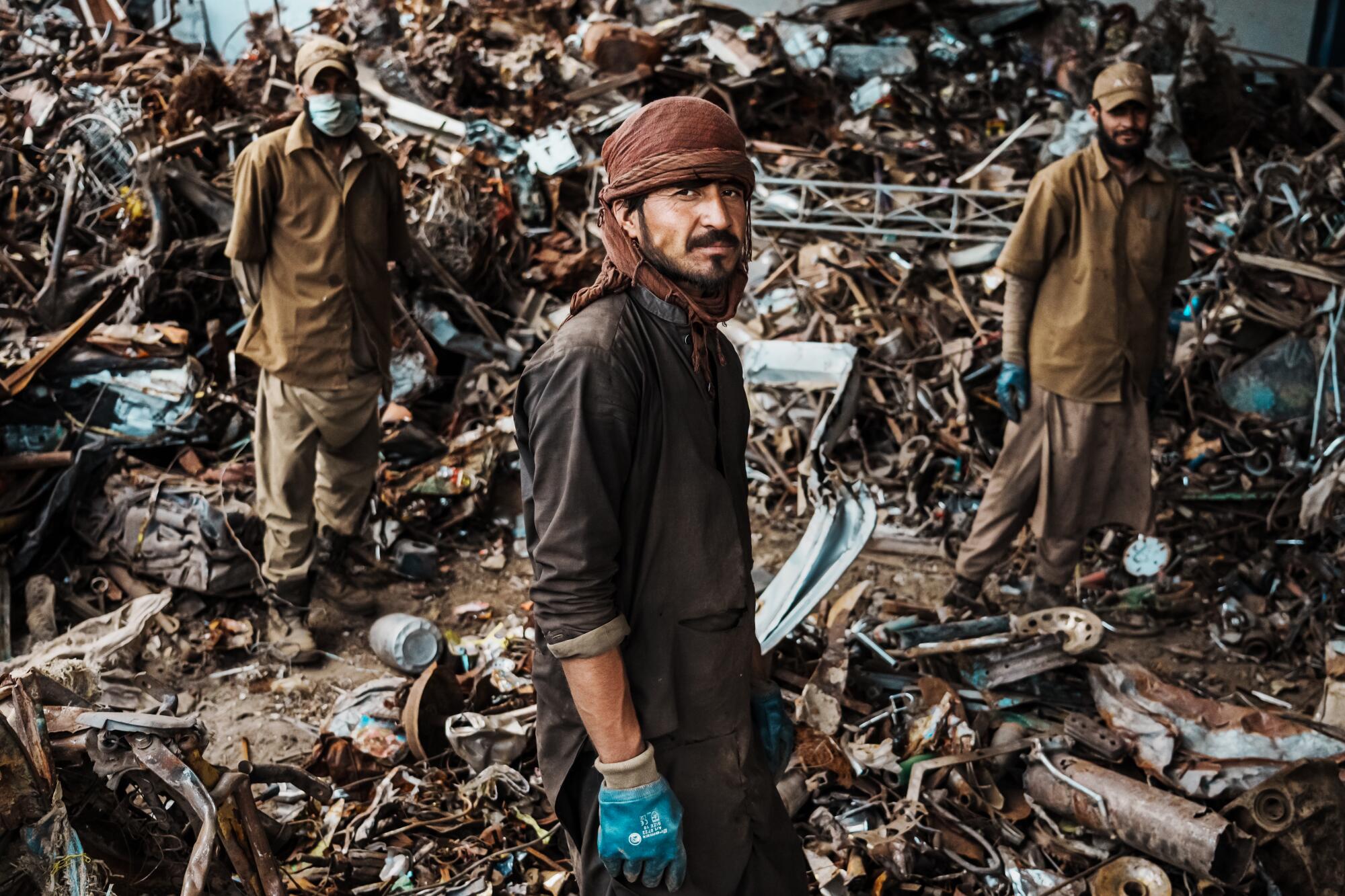 Workers wearing gloves sort through a big pile of metal parts