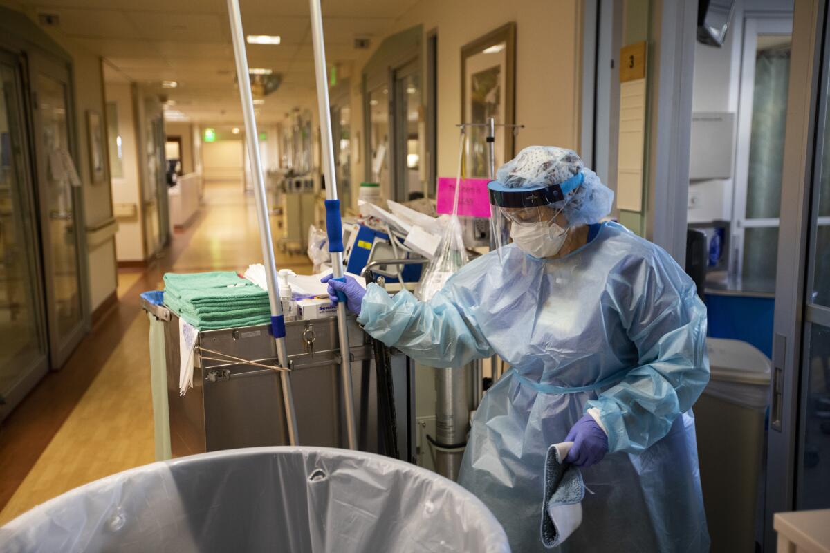 A worker in protective gear mans a cleaning cart at a hospital 