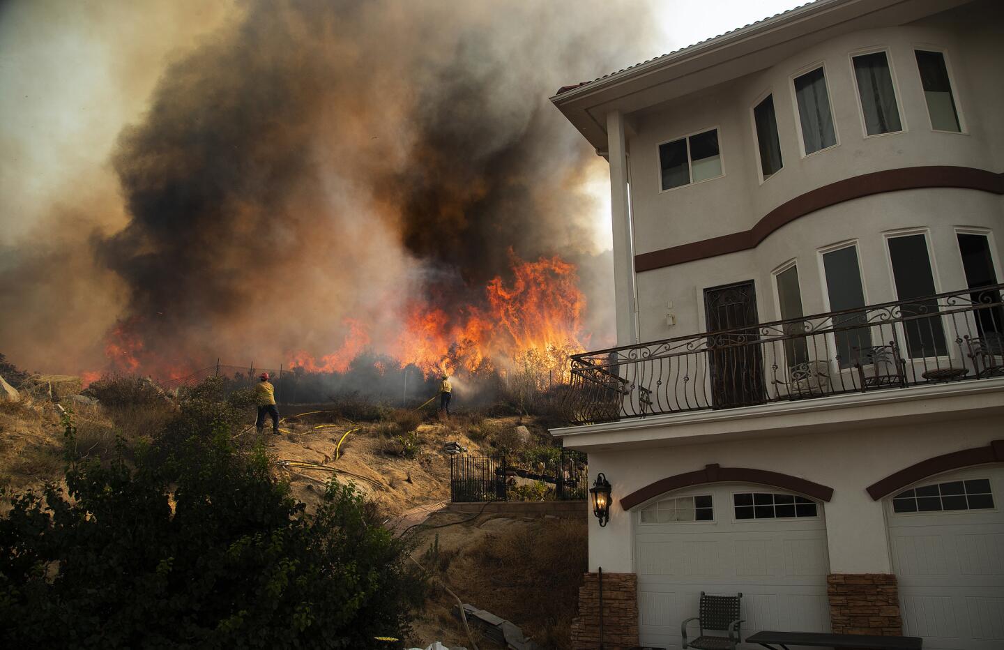 Afternoon winds fan flames close to a home north of Grand Avenue in Lake Elsinore, Calif.