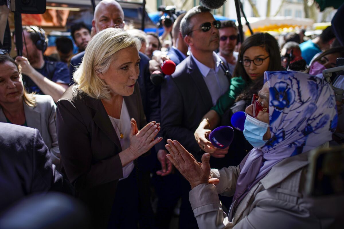 French far-right leader Marine Le Pen, left, talks to a woman as she campaigns in a market in Pertuis, southern France, Friday, April 15, 2022. (AP Photo/Daniel Cole)
