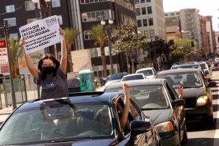 LOS ANGELES, CA - FEBRUARY 20, 2021 - - Garfield High School Senior Ishmeray Coronado, 18, holds a sign that translate to, "Until schools are safe, invest more to make distance learning work now," while joining her sister Genesis Coronado, 28, driving, and demonstrators in a car caravan to not force Los Angeles county school re-openings until safe in front of outside of the Ronald Reagan State Office Building in downtown Los Angeles on February 20, 2021. Parents, students, educators, and community members concerned with calls from Governor Newsom and local politicians to return to in-person schooling demanding for stronger safety measures and an end to educational racism. The "Not My Child: Schools Are Not Safe" demonstration want all school staff having access to vaccinations; smaller class sizes to ensure social distancing; necessary sanitation and PPE; and for every zip code in LAUSD to be out of the purple tier. (Genaro Molina / Los Angeles Times)