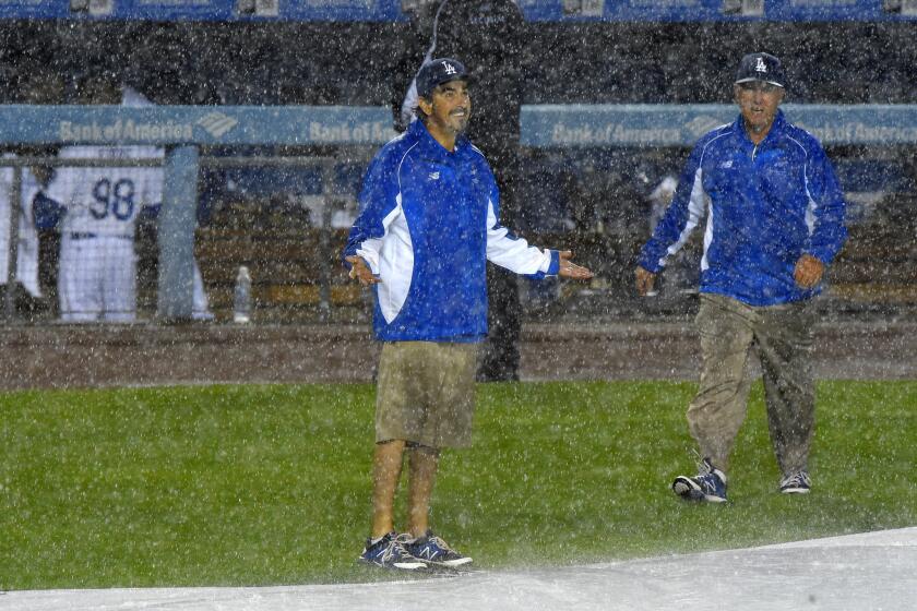 Grounds crew members get caught in the downpour while putting down the tarp during a rain delay at Dodger Stadium on Thursday night.
