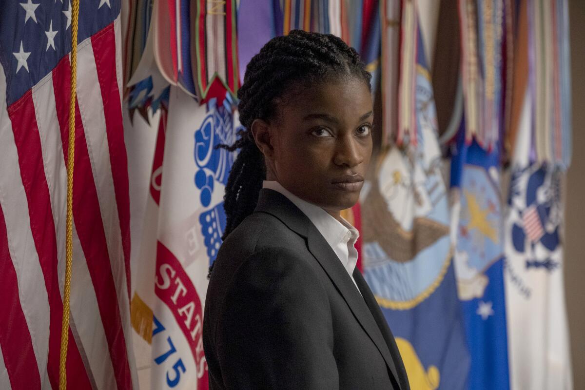 A woman Secret Service agent stares at the camera before a wall of flags.
